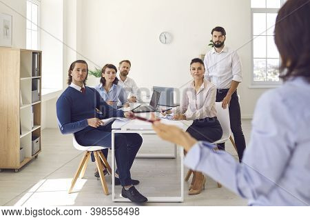 Group Of Office Workers Sitting And Listening To Colleague Making Presentation In Office