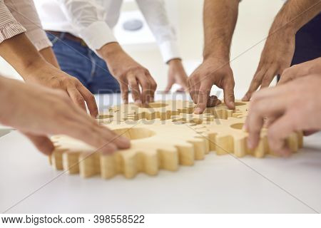 Hands Of Business People Making Whole Picture Of Wooden Gears On Table Together
