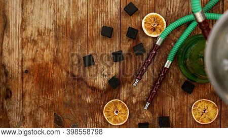Coals For Hookah On Wooden Background With Dry Oranges And Hookah Pipes. Place For Text