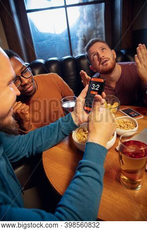 Tensioned. Excited Fans In Bar With Beer And Mobile App For Betting, Score On Their Devices. Screen 