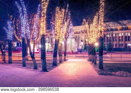 Winter Park At Night With Christmas Decorations, Lights, Pavement And Trees.