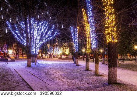 Winter Park At Night With Christmas Decorations, Lights, Pavement And Trees.