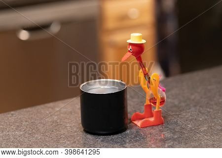 A Dipping Bird Drinking Toy Sits On The Counter With A Cup Of Water