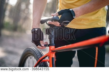 Rider adjusting seat height on bicycle standing in sunny forest