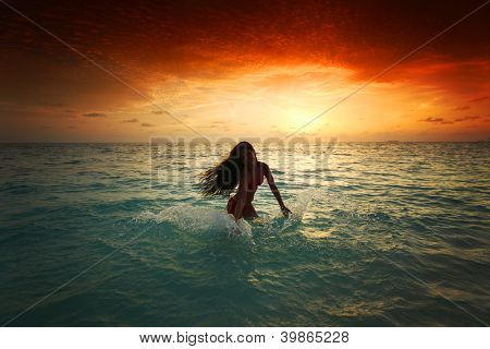 Vrolijke vrij jonge vrouw splashin in zee op zonsondergang