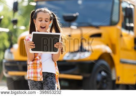 Adorable Little Schoolgirl Near School Bus And Looking At Camera
