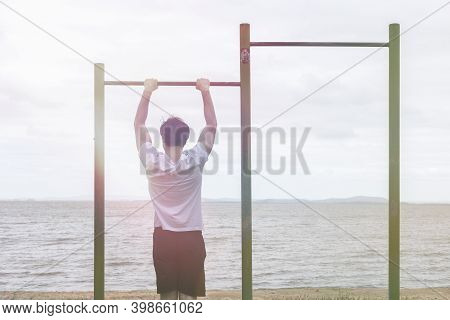 Boy Doing Exercises On The Bar At The Beach - Healthy Concept - Sunlight