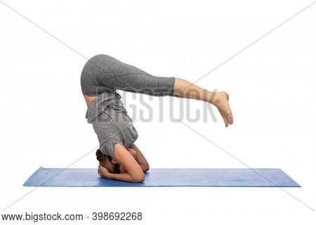 fitness, sport, people and healthy lifestyle concept - woman making yoga in headstand pose on mat