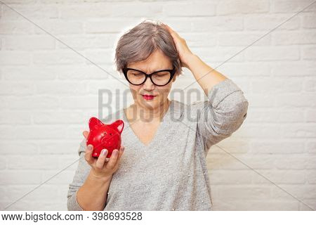Sad Elderly Woman With Red Piggy Bank On White Background. Unsustainability Of Social Transfers And 