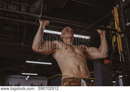 Low Angle Shot Of A Sexy Ripped Shirtless Athlete Doing Pull-ups On A Bar At The Gym. Muscular Sport