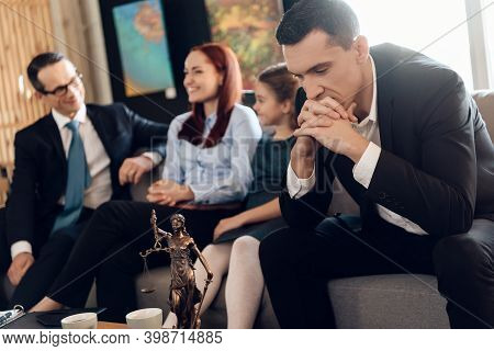 Frustrated Father, With Arms Crossed, Sits On Couch Next To Young Wife And Daughter.