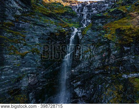Long Narrow Waterfall Cutting Through The Terrain On A Steep Green Mountain Slope. 4k Aerial Footage