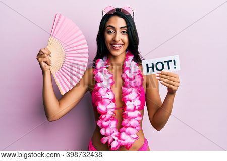 Beautiful hispanic woman wearing bikini and handfan holding hot word smiling and laughing hard out loud because funny crazy joke. 