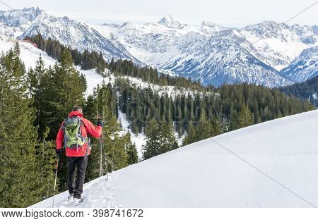 Senior Man Is Snowshoe Hiking In Alpine Snow Winter Mountains. Allgau, Bavaria, Germany.