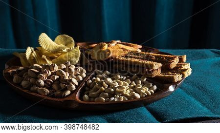 Beer Snacks Set On The Wooden Plate: Pistachios, Peanut, Chips, Fried White Bread, Cronuts, Food Und
