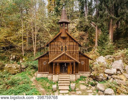 Wooden Pilgrimage Rural Chapel Of Virgin Mary, Cz: Stozecka Kaple And Iron Cross Standing In Forest 