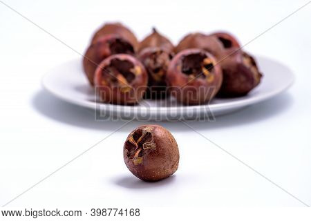 Fresh Ripe Organic Common Medlar Fruit  On White Background With More Medlars On A Plate In The Back