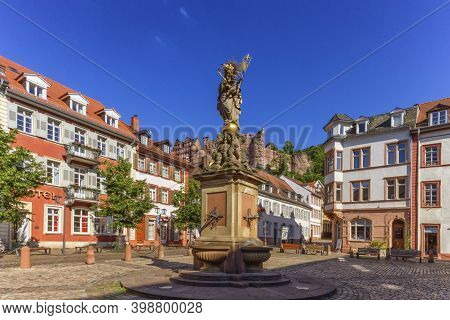 The Madonna Statue In Kornmarkt Square And Castle In Heidelberg By Day, Germany