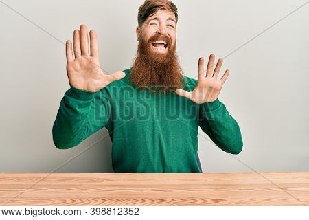 Young irish redhead man wearing casual clothes sitting on the table afraid and terrified with fear expression stop gesture with hands, shouting in shock. panic concept. 