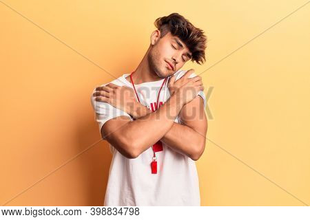 Young hispanic man wearing lifeguard t-shirt and whistle hugging oneself happy and positive, smiling confident. self love and self care 
