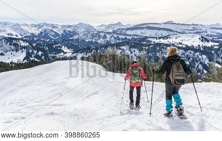 Senior Couple Is Snowshoe Hiking In Alpine Snow Winter Mountains. Allgau, Bavaria, Germany.