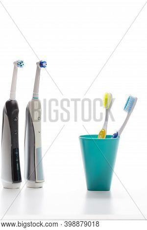 Professional Electric Toothbrushes In Front Of Two Manual Tooth Brushes In One Cup On White Backgrou