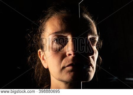 Dark Portrait Of A Serious Woman With Only Half Her Face Illuminated On A Black Background That Is U