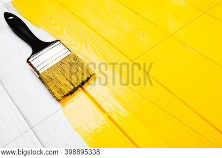Paintbrush Is Applying On Yellow Half Freshly Painted Wooden Background. Repairing Concept.