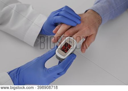 Doctor Checking Patient's Oxygen Level With Pulse Oximeter At Light Grey Table, Closeup