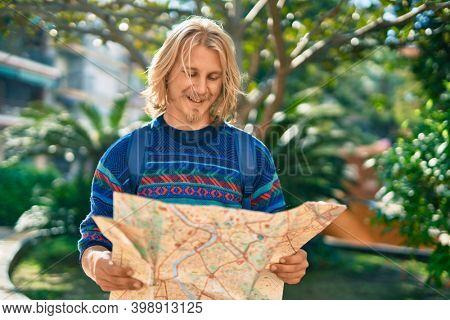 Young scandinavian tourist man smiling happy using map at the park.
