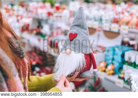 The Girl Holds Tomte In Her Hands. Against The Background Of The Counter Of The Christmas New Year's