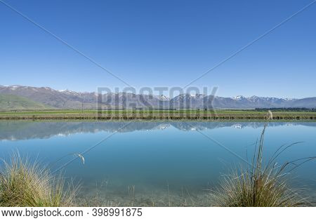 View Across Calm Clear Water Of Ohau Canal To Surrounding Landscape At Sunrise.