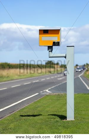 UK static speed camera with speeding cars approaching on a rural road