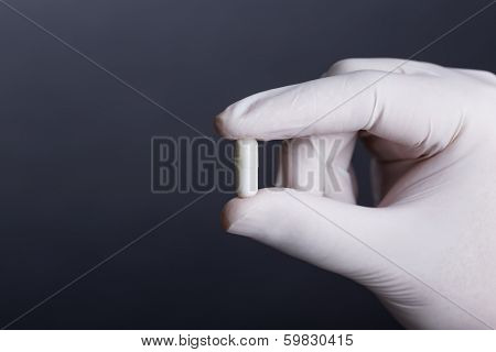Hand in white latex glove holding white capsule