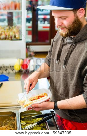 Hotdog - friendly salesman and fresh ingredients in a fast food snack bar