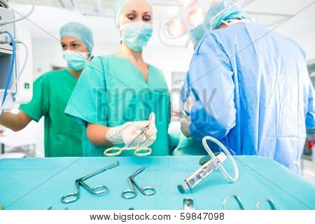 Hospital - surgery team in the operating room or Op of a clinic operating on a patient, perhaps it's an emergency a assistant holding a cotton swap forceps