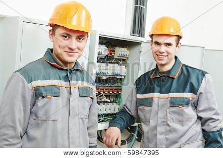 Happy young adult electrician builder engineer workers in front of fuseboard