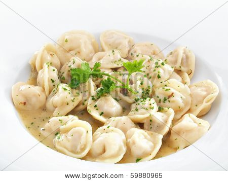 Traditional Russian dumplings with meet or cheese served with parsley on a white round plate. Isolated on white.
