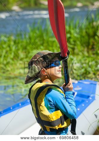 Happy young boy holding paddle near a kayak