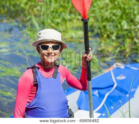 Happy cute girl holding paddle near a kayak