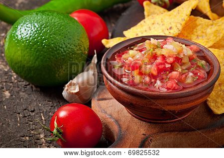 Mexican nacho chips and salsa dip in bowl on wooden background