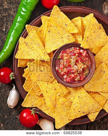 Mexican nacho chips and salsa dip in bowl on wooden background