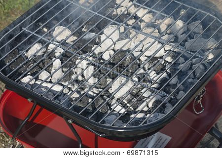 Portable BBQ with burning charcoal and smoke.