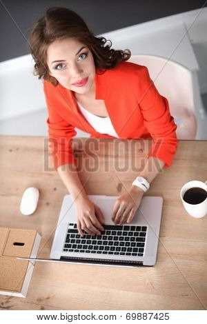 Attractive woman sitting at desk in office, working with laptop computer