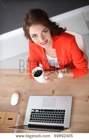 Attractive woman sitting at desk in office, working with laptop ,holding a cup