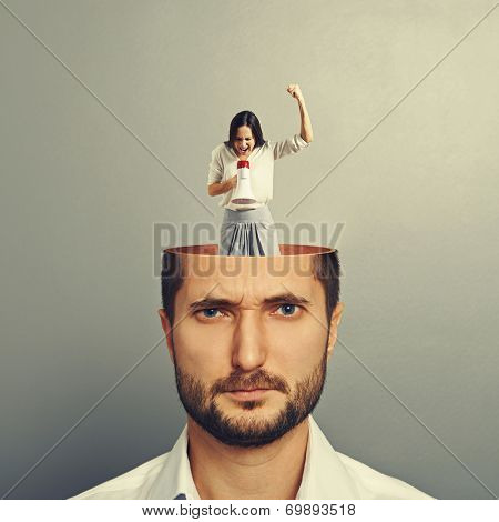 young man with open head. small angry woman standing in the man's head and screaming with megaphone. photo over grey background