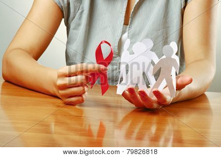 A woman holding paper peolple and an aids red ribbon