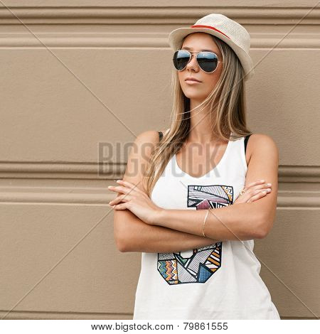 Girl In Sunglasses And A Hat Stands Near The Wall
