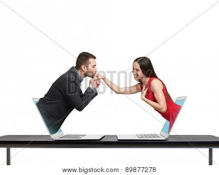 concept of love in social network. young man got out of the computer and kissing hand of beautiful young woman who got out of another computer over white background