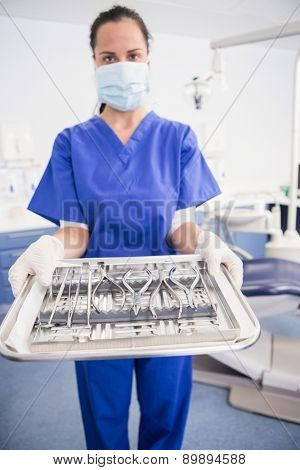 Portrait of a dentist with surgical mask and holding tray in dental clinic